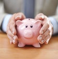 Protecting his assets. Cropped image of a businessmans hands covering a piggybank.