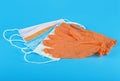 Protection concept - pair of orange latex medical gloves and colored surgical masks on blue background Royalty Free Stock Photo