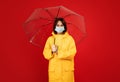 Protection concept. Portrait of young lady wearing raincoat and face mask, standing under umbrella, red background Royalty Free Stock Photo