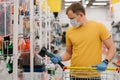 Protection from coronavirus. Man chooses ax in building department of shopping mall, poses with shopping cart, wears disposable