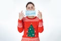 Protection from coronavirus. A young woman with a stupid expression in her eyes, wearing a Christmas sweater, holds a medical mask