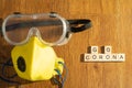 Protective eyewear and yellow mask with outlet valve with wooden blocks spelling out go corona go on a wood floor
