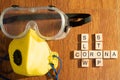 Protective eyewear and yellow mask with outlet valve with wooden blocks spelling out Slow corona stop on a wood floor