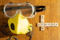 Protective eyewear and yellow mask with outlet valve with wooden blocks spelling out slow corona on a wood floor
