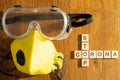 Protective eyewear and yellow mask with outlet valve with wooden blocks spelling out stop corona on a wood floor