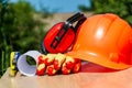 Protective hard hat, headphones, gloves, glasses and roulette on wooden background, copy space Royalty Free Stock Photo