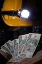 A protective helmet with a glowing flashlight and paper money of one hundred zloty denomination lies on the black coal