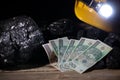 A protective helmet with a glowing flashlight and paper money of one hundred zloty denomination lies on the black coal