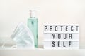 Protective mask and antibacterial gel or soap and PROTECT YOURSELF written on light board. Protecting yourself and others during