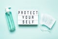 Protective mask and antibacterial gel or soap and PROTECT YOURSELF written on light board. Protecting yourself and others during