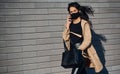 In protective mask. Beautiful brunette with curly hair and in black clothes talking by phone outdoors near wall Royalty Free Stock Photo