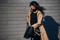 In protective mask. Beautiful brunette with curly hair and in black clothes talking by phone outdoors near wall Royalty Free Stock Photo