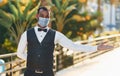 In protective mask. Black waiter in formal clothes is at his work outdoors at sunny daytime Royalty Free Stock Photo