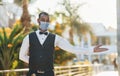 In protective mask. Black waiter in formal clothes is at his work outdoors at sunny daytime Royalty Free Stock Photo