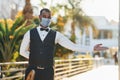 In protective mask. Black waiter in formal clothes is at his work outdoors at sunny daytime Royalty Free Stock Photo
