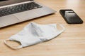 A protective mask, smartphone and a laptop are on the desk. Organization of workplace during coronavirus outbreak. Royalty Free Stock Photo