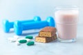 Protein bar, glass of protein shake with milk and raspberries. BCAA amino acids, L - Carnitine capsules and blue dumbbells in back Royalty Free Stock Photo