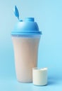A protein shake and a scoop on blue background, front view Royalty Free Stock Photo