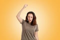 Protest. A young Caucasian woman shouts with displeasure, raising her hand up. Yellow background. The concept of aggressive