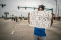 Black lives matter protester standing on a closed street with a no justice no peace sign