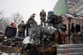 Protesters with hidden faces guard on the top of burned and smashed buses on winter street during anti-government protest