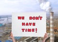 Protestor holding placard with text We Don`t Have Time and blurred view of industrial factory on background. Climate strike