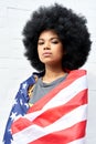 Proud African woman stand on white background wrapped in usa flag, portrait.