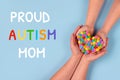 Proud Autism Mom and World Autism Awareness Day concept - autistic child`s hands supported by mother holding multicolored heart o