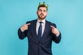 Proud bearded man wearing official style suit egoistically looking at camera, posing with crown on