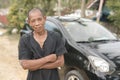 A proud car owner in a black shirt posing in front of his vehicle. Flaunting his belongings earned from his farming business