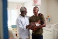 Proud Grandfather With Adult Son Cuddling Baby Grandson In Nursery At Home