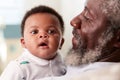 Proud Grandfather Cuddling Baby Grandson In Nursery At Home