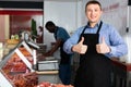 Proud male owner of butcher shop standing behind counter, giving thumbs up Royalty Free Stock Photo