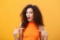 Proud and satisfied cool urban female with red lipstick and curly hairstyle pointing at herself with self-assured