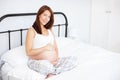 Proudly expecting. Portrait of a beautiful pregnant woman holding her baby bump while sitting in bed. Royalty Free Stock Photo