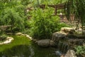 Stone boulders and a waterfall with a wooden fence and a gazebo for relaxing among the trees in the World of Birds Park in Tehran.