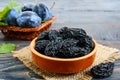 Prunes in a clay bowl and fresh plums, leaves on a wooden table.