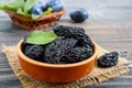 Prunes in a clay bowl and fresh plums, leaves on a wooden table. Royalty Free Stock Photo