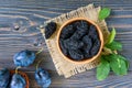 Prunes in a clay bowl and fresh plums, leaves on a wooden table. Royalty Free Stock Photo