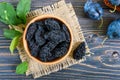 Prunes in a clay bowl and fresh plums, leaves on a wooden table Royalty Free Stock Photo