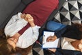 Psychologist listening to young depressed female patient lying on sofa and writing notes, top view, mental health and Royalty Free Stock Photo