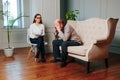 Psychologist woman and sick senior man sit in large cozy office.