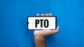 PTO word on smart phone screen isolated on blue background with copy space for text. Paid time off Royalty Free Stock Photo