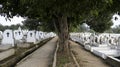 The public cemetery pathway contains identical white ceramic graves at the left and right