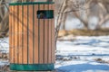 Public garbage can with green metal and wood planks - in winter with snow around it
