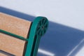 Public green and wood park bench with shadow on white snow