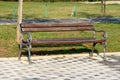 Public park bench with wooden boards and baroque style wrought iron supports mounted on black and grey stone tiles with grass and