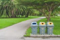 Public recycle bins or segregated waste bins sitting on concrete floor beside walkway in public park.