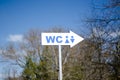 WC direction plate. Toilet signpost on the background of trees and sky.