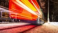 Public transportation in a city. Tram leaving the station, traffic lights, people, street, houses, overhead wires, rails. Movement